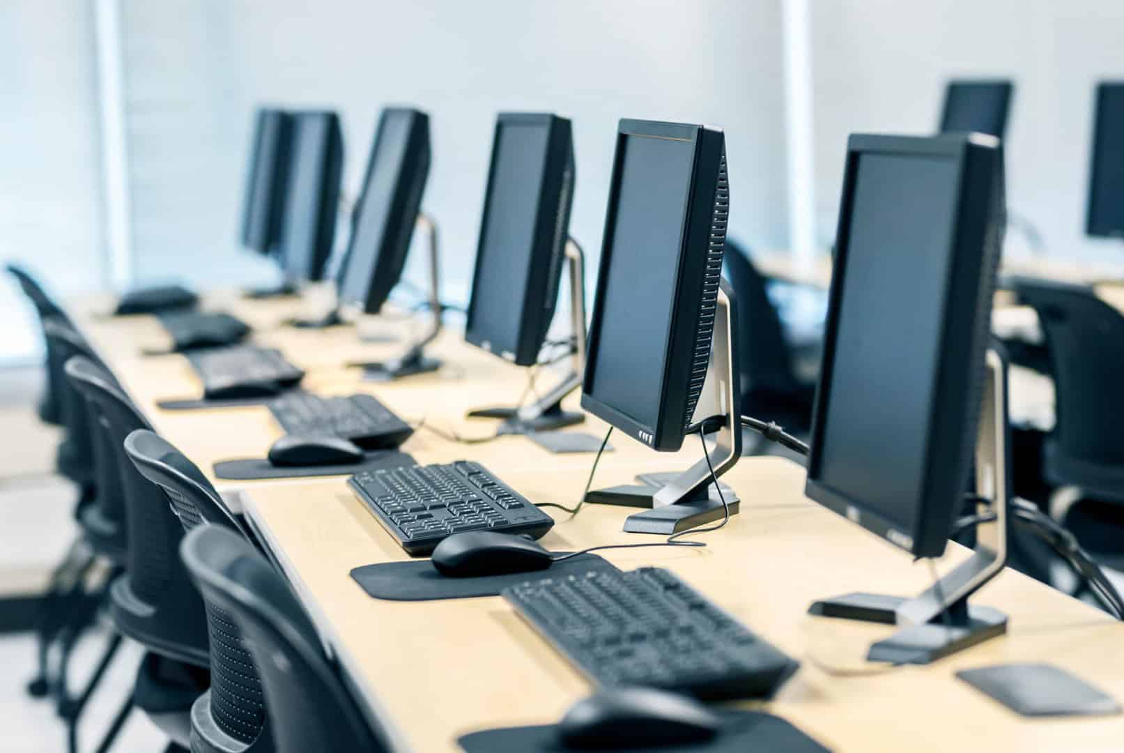 modular ICT suite. Rows of desktop computers with monitors, keyboards, and mice, are placed on long tables in a brightly lit, modern classroom or office setting.