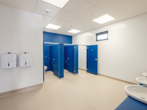 Image shows a spacious restroom with blue doors on the stalls.