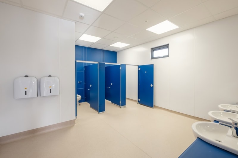 Image shows a spacious restroom with blue doors on the stalls. 